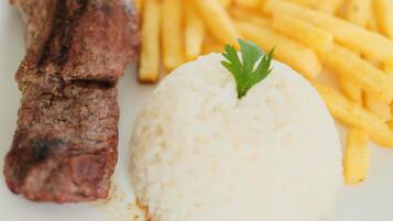 Un plato con un trozo de carne a la parrilla, papas fritas y una porción de arroz coronada con una ramita de perejil.
