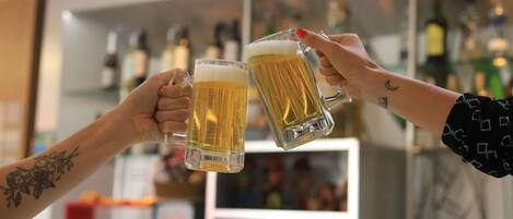 Two people toasting with beer mugs in a bar setting with shelves of bottles in the background.
