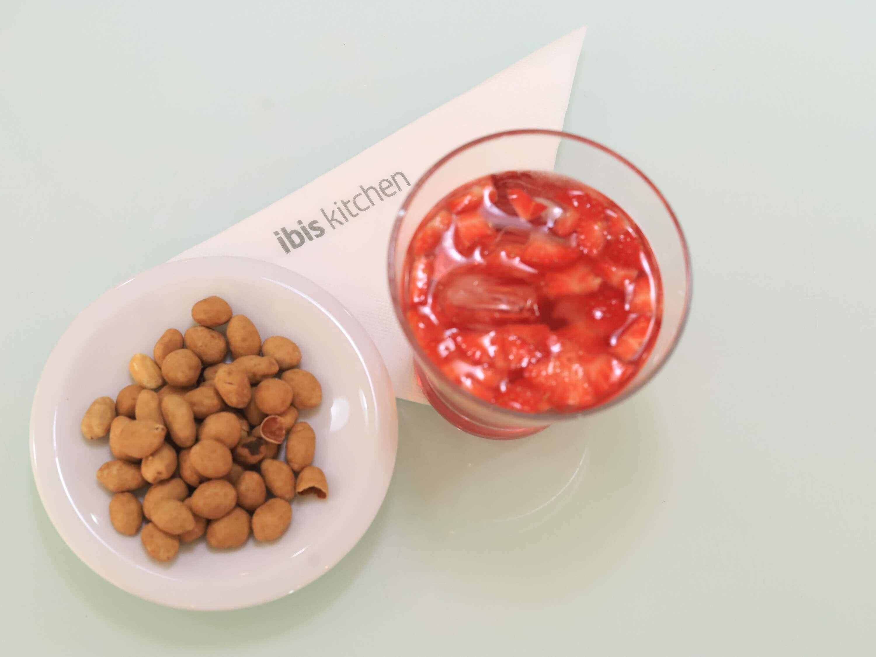 Un plato blanco con cacahuates y un vaso de puré de frutos rojos.