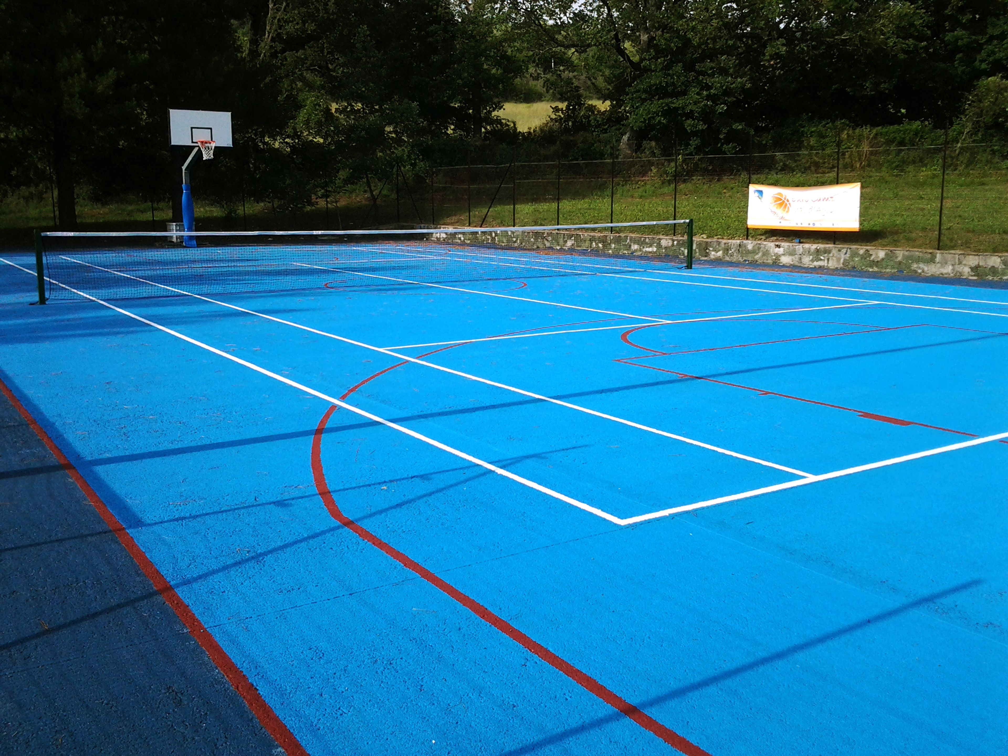 An outdoor basketball court with blue flooring and white boundary lines.