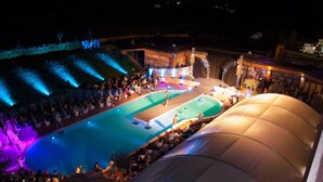 Un événement en plein air comprenant une scène et des places assises pour le public, une piscine et une grande structure en forme de tente.