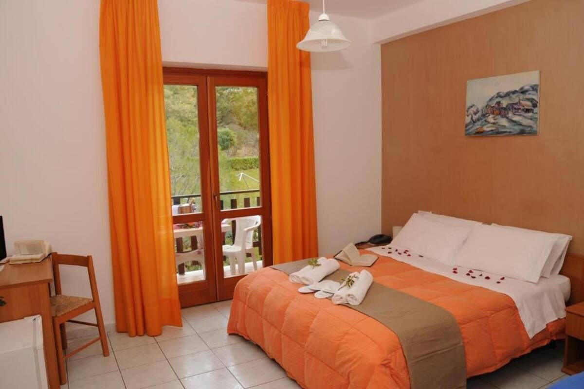 Un dormitorio con una cama, un escritorio y una silla. Cuenta con un balcón con cortinas naranjas.