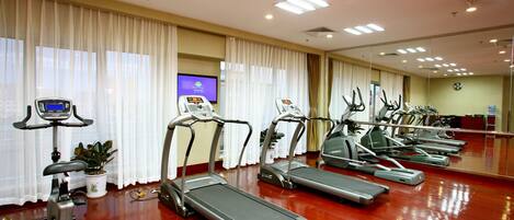A gym with multiple treadmills, exercise bikes, and a television screen displaying a workout program.