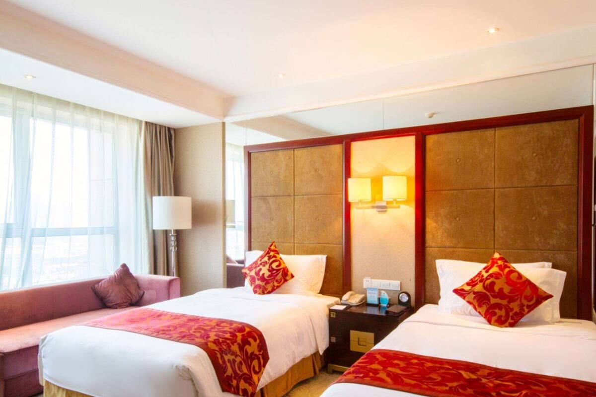 Ein Hotelzimmer mit zwei Betten, einem Schlafsofa, einem Nachttisch mit Telefon und einem Fenster mit Vorhängen.