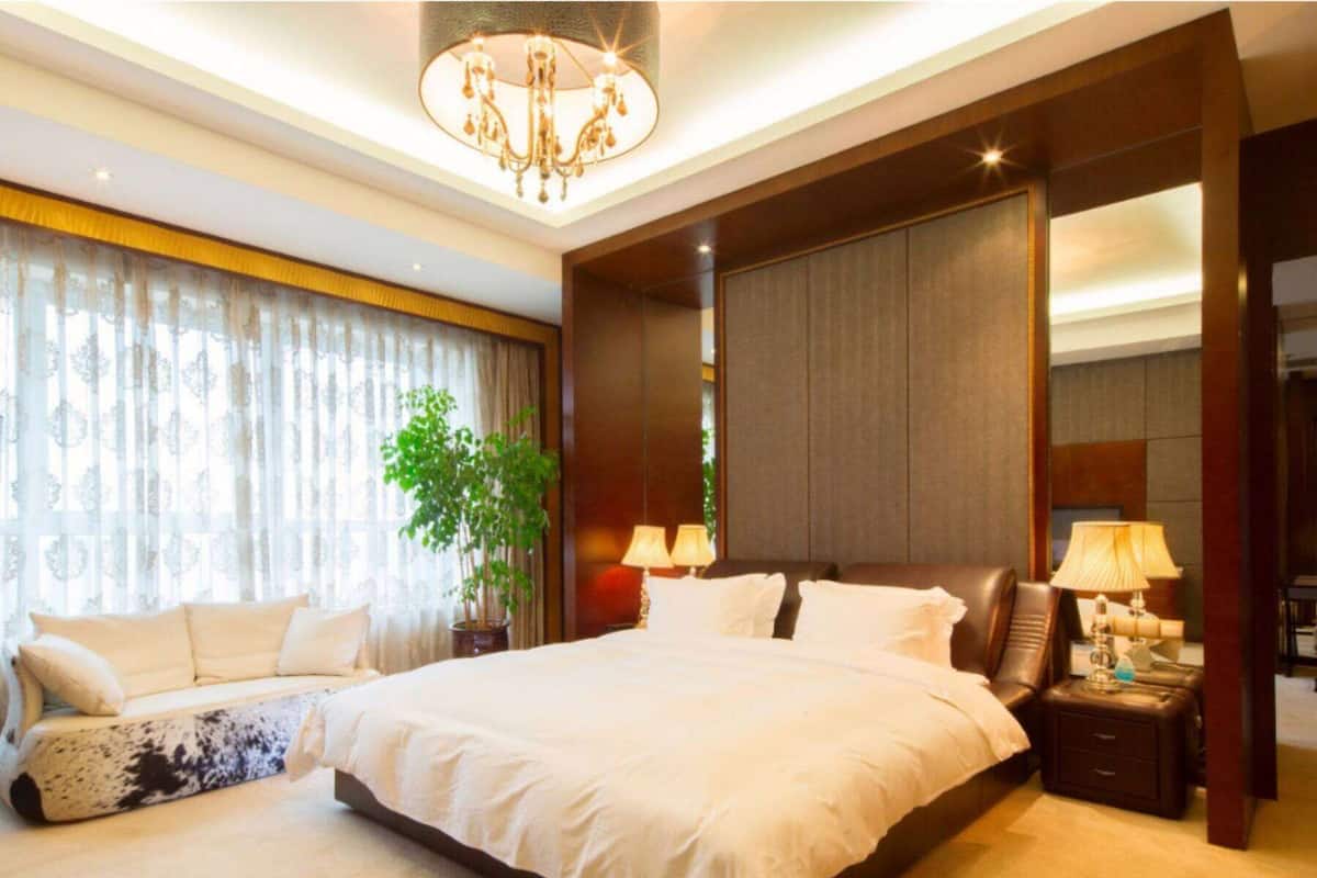 Ein geräumiges Schlafzimmer mit einem großen Bett, zwei Nachttischen mit Lampen, einer Kristallleuchtre und einem Blumentopf.