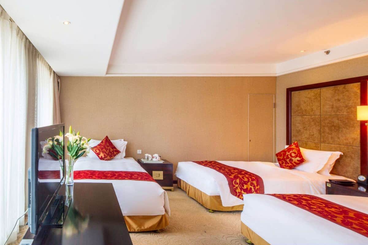 Ein Hotelzimmer mit zwei Betten, einem Nachttisch, einem Schreibtisch und einer Vase mit Blumen.