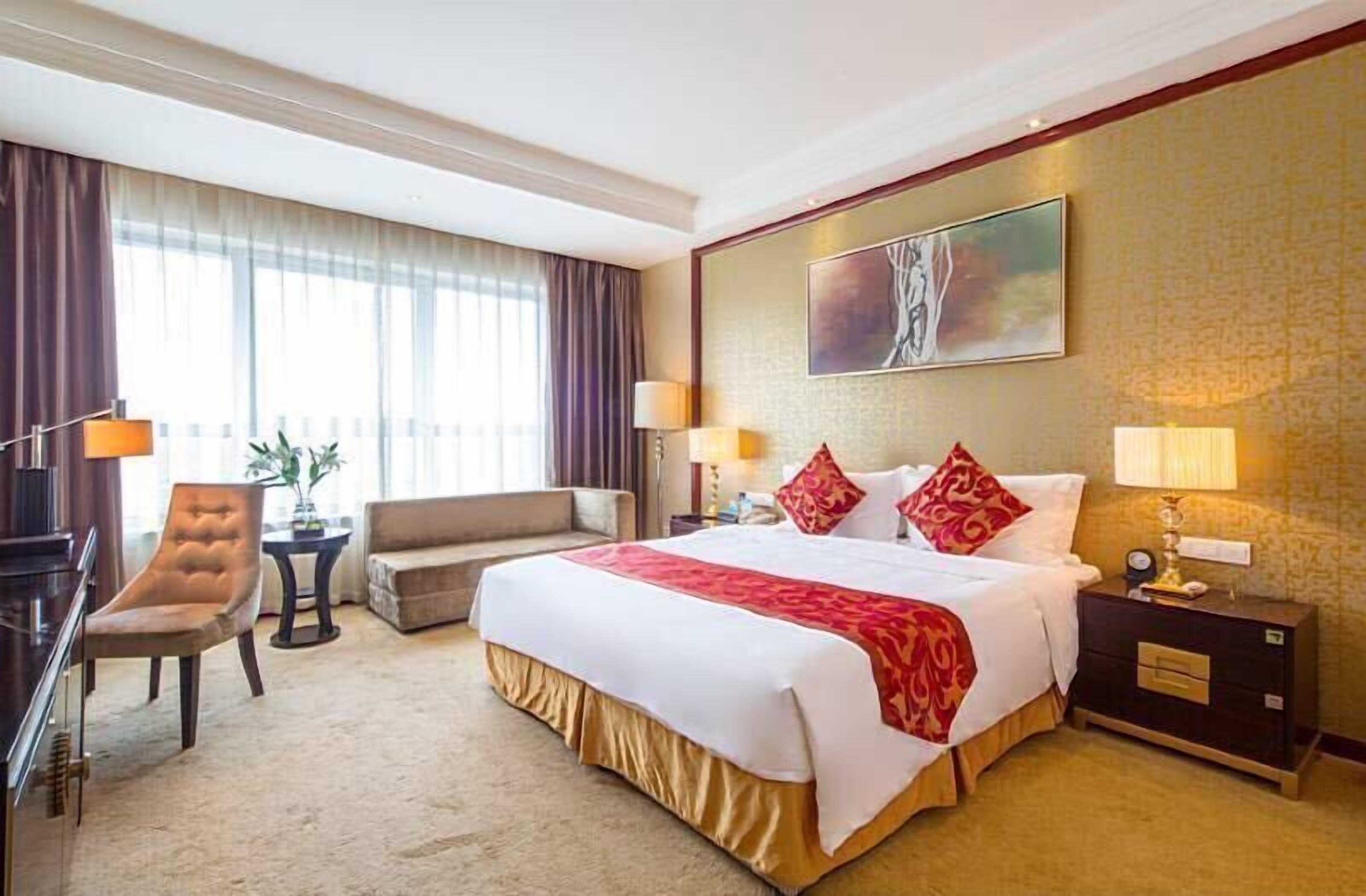 A hotel room with a large bed, two bedside tables, a desk, a chair, and a sofa.