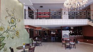 A spacious indoor area with multiple dining tables and chairs, a decorative wall with floral patterns, a chandelier, and a staircase leading to an upper level. - Ararat Hotel (Bethlehem)