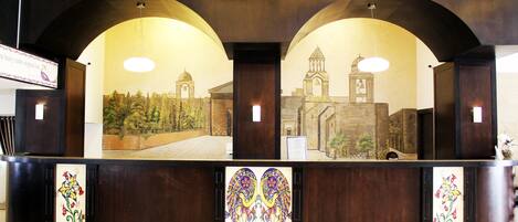 Una recepción con un mural de un edificio histórico, paneles de madera y diseños florales decorativos.