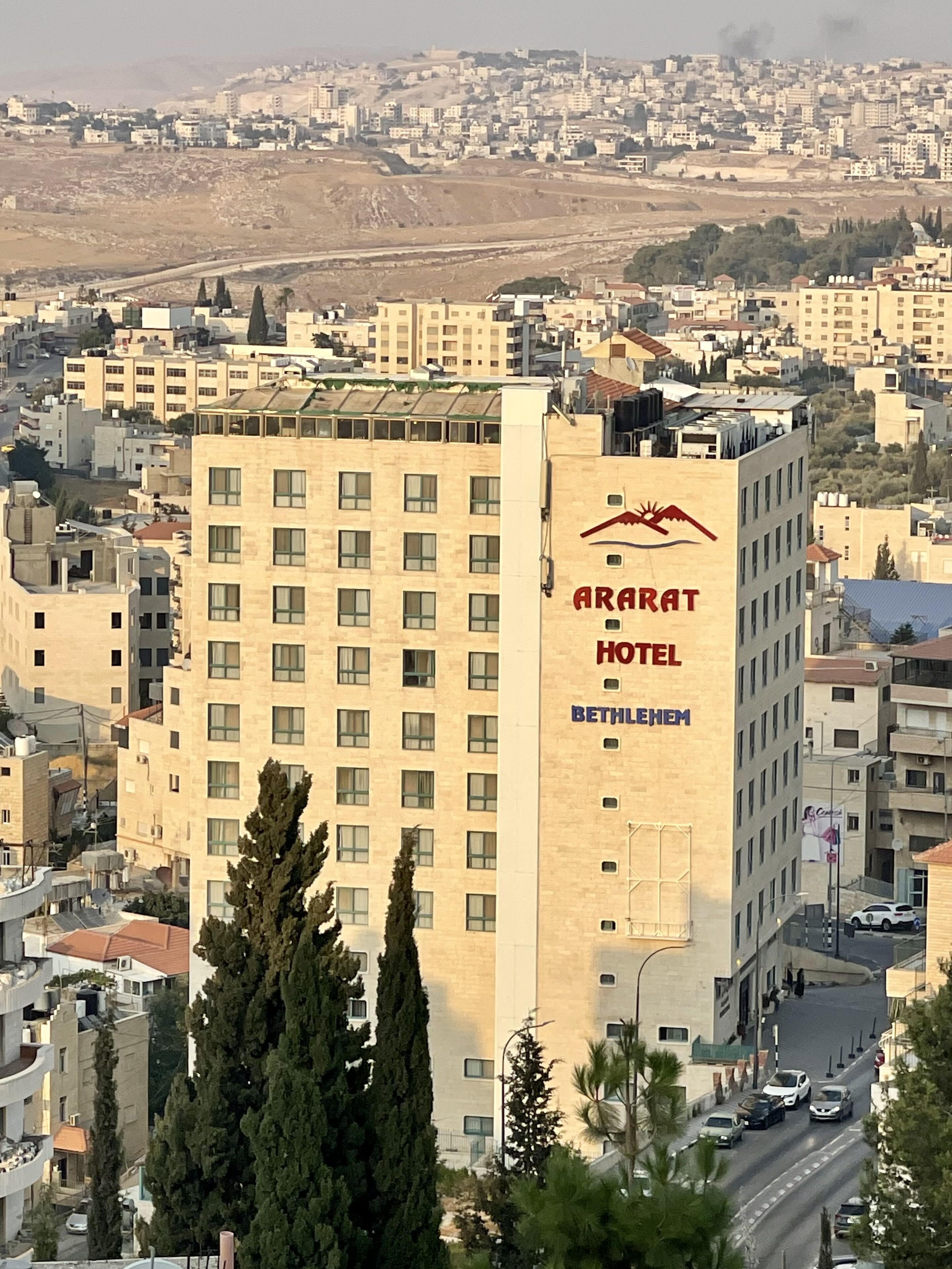 A hotel building with a sign reading "ARARAT HOTEL BETHLEHEM" and a view of the surrounding cityscape.