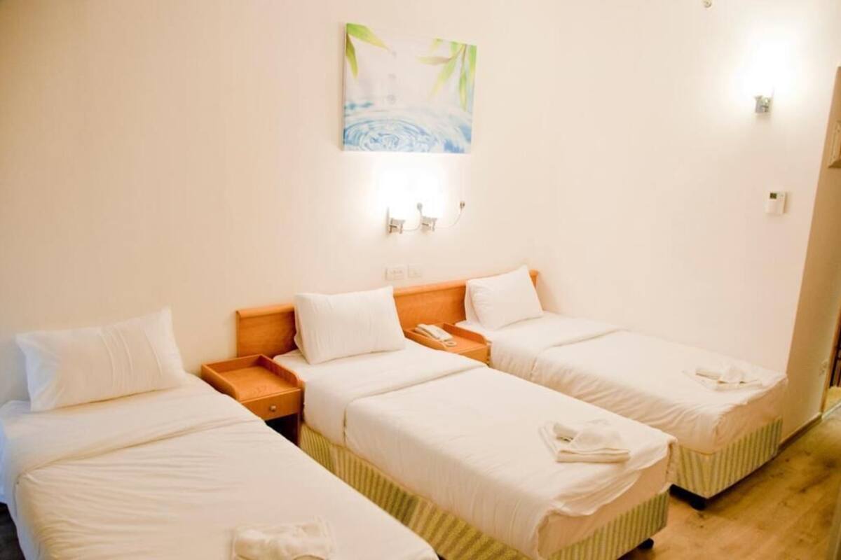 Une chambre d’hôtel avec trois lits simples, une table de chevet en bois, un téléphone et un tableau au mur.