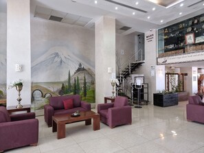 A spacious lobby with a mural of a mountain and a bridge, purple seating, and a souvenir store. - Ararat Hotel (Bethlehem)