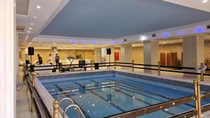 A large indoor swimming pool with clear water, surrounded by a poolside area with a railing. - Ararat Hotel (Bethlehem)