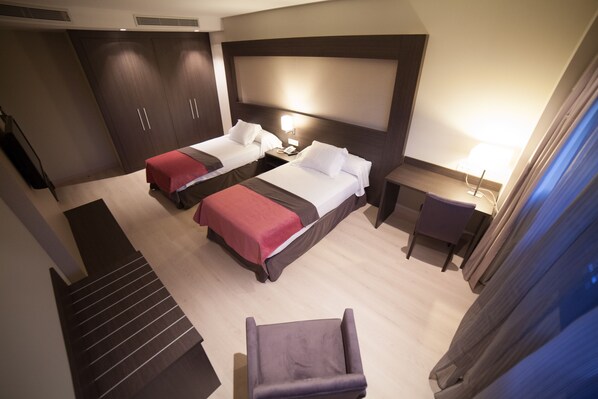 Habitación de hotel con dos camas, un escritorio, una silla y una escalera.