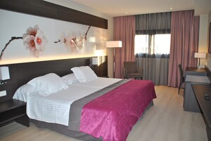 Habitación de hotel con una cama grande, un escritorio, una silla y un ventanal con cortinas.