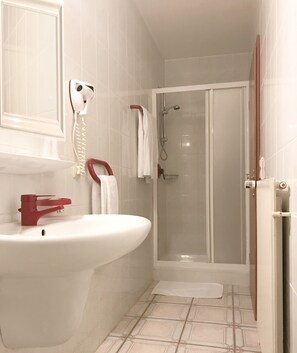 A bathroom with a white sink, a red faucet, a towel rack, a shower with a glass door, and a toilet paper holder. - Hôtel Carpini (Käerjeng)