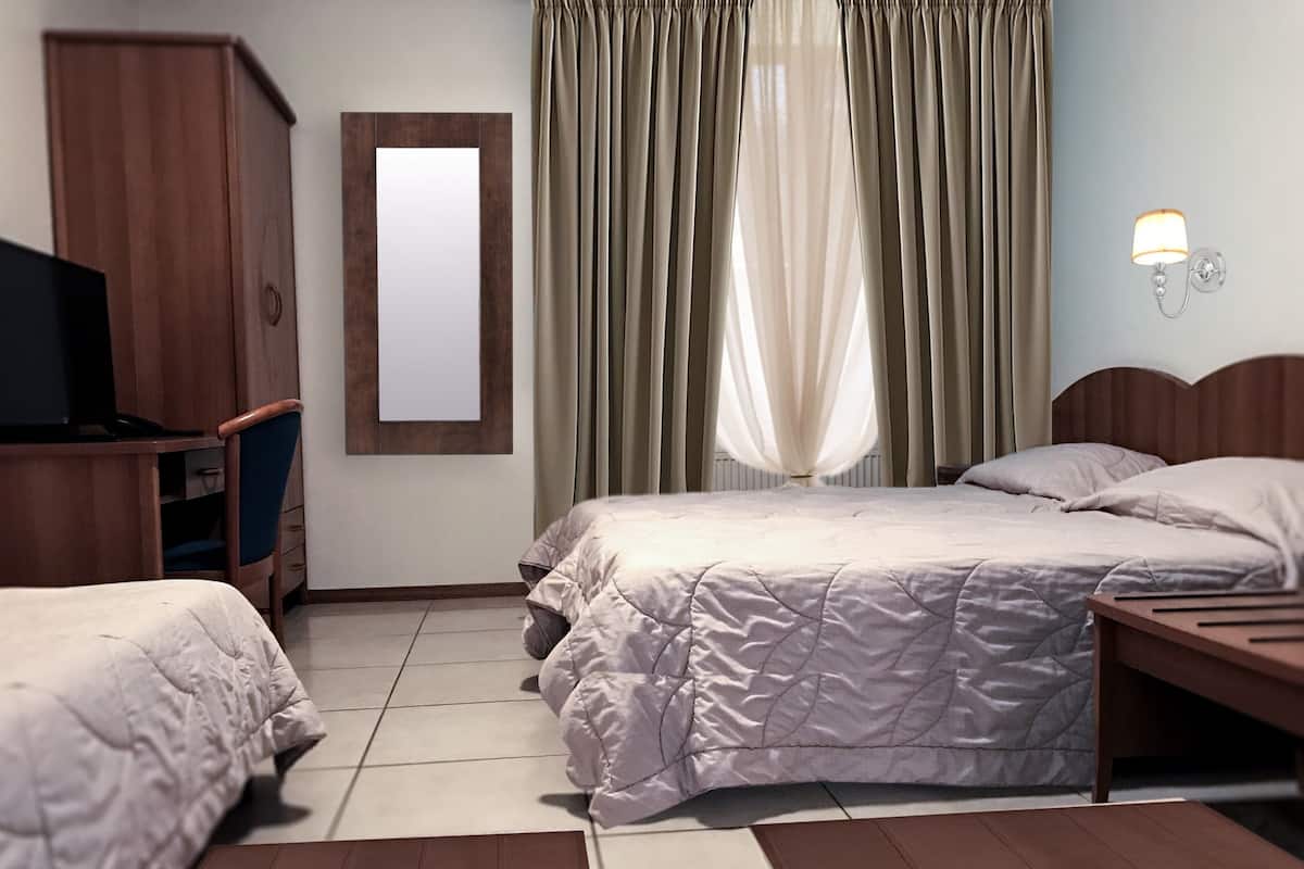 Quarto de hotel com cama, televisão, guarda-roupa e janela com cortinas.
