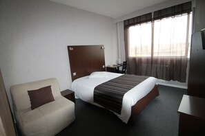 Une chambre d’hôtel avec un lit, une chaise, un bureau et un téléviseur.