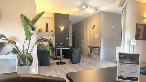 A modern hotel room with a dining area, a black leather chair, a table with a menu, and a potted plant. - Adonis Lyon Est Hôtel Artys (Saint-Priest)