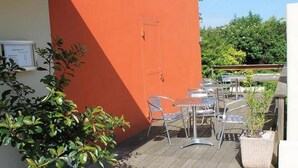 A patio with metal tables and chairs, a potted plant, and a door on a building with an orange wall. - Adonis Lyon Est Hôtel Artys (Saint-Priest)