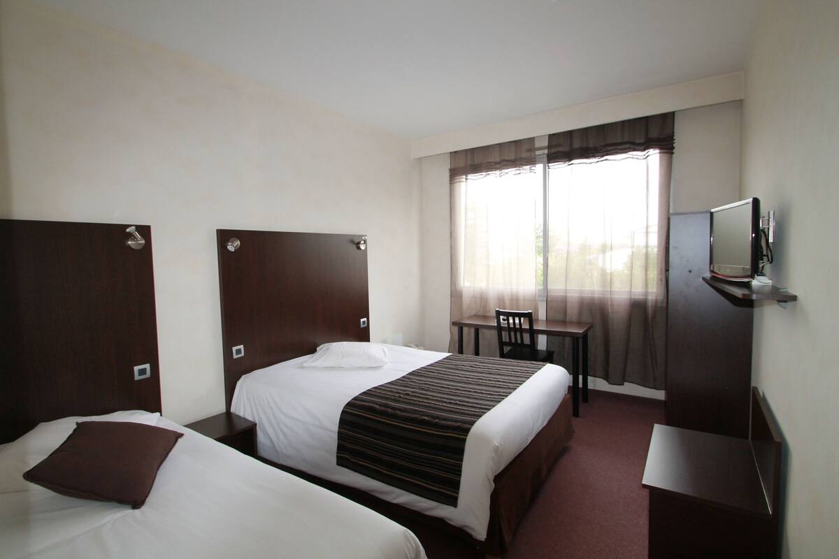 A hotel room with two beds, a desk, a chair, and a television.