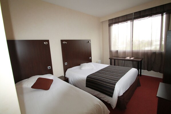 Una habitación de hotel con dos camas, un escritorio y un amplio ventanal con cortinas.