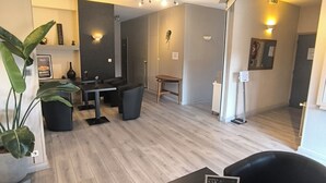 A modern hotel room with a dining area, a small table with a menu, a potted plant, and a mirror on the wall. - Adonis Lyon Est Hôtel Artys (Saint-Priest)