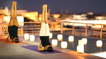 Two people performing a handstand on a yoga mat by a poolside at night.