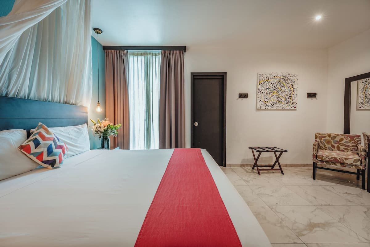 A hotel room with a bed, a chair, a small table, and artwork on the walls.