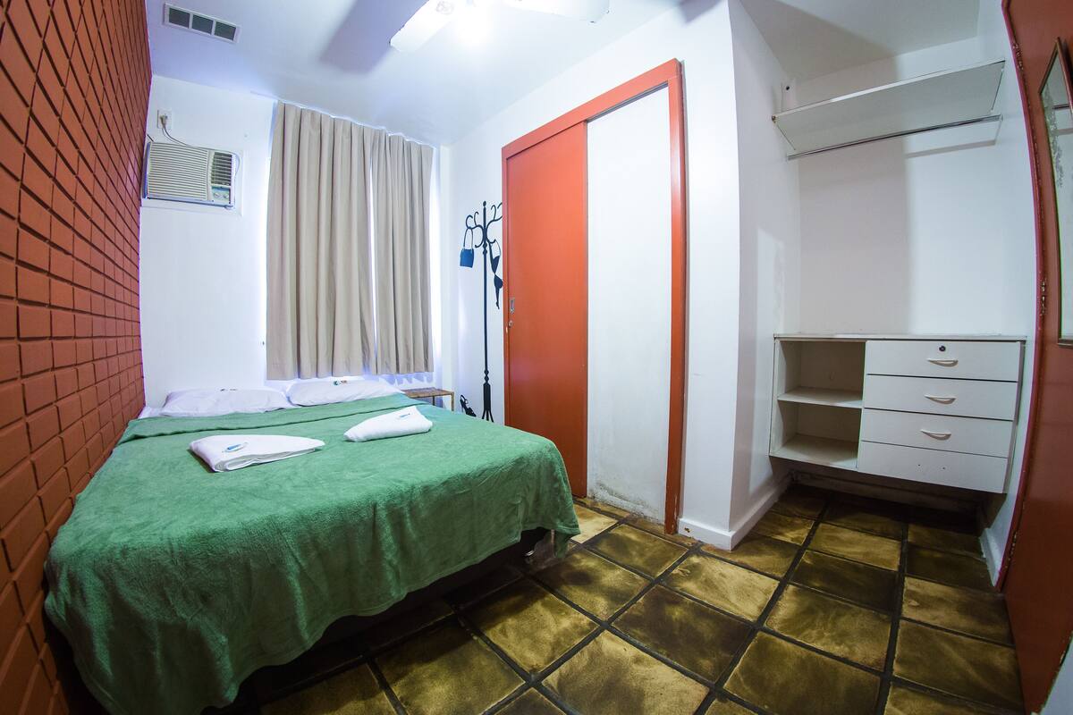 A hotel room with a bed, a wardrobe, a mirror, and a window with curtains.