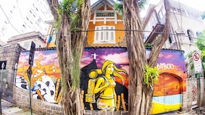 Une fresque colorée représentant une femme et un enfant, une croix et une enseigne en bambou, le tout peint sur un bâtiment.