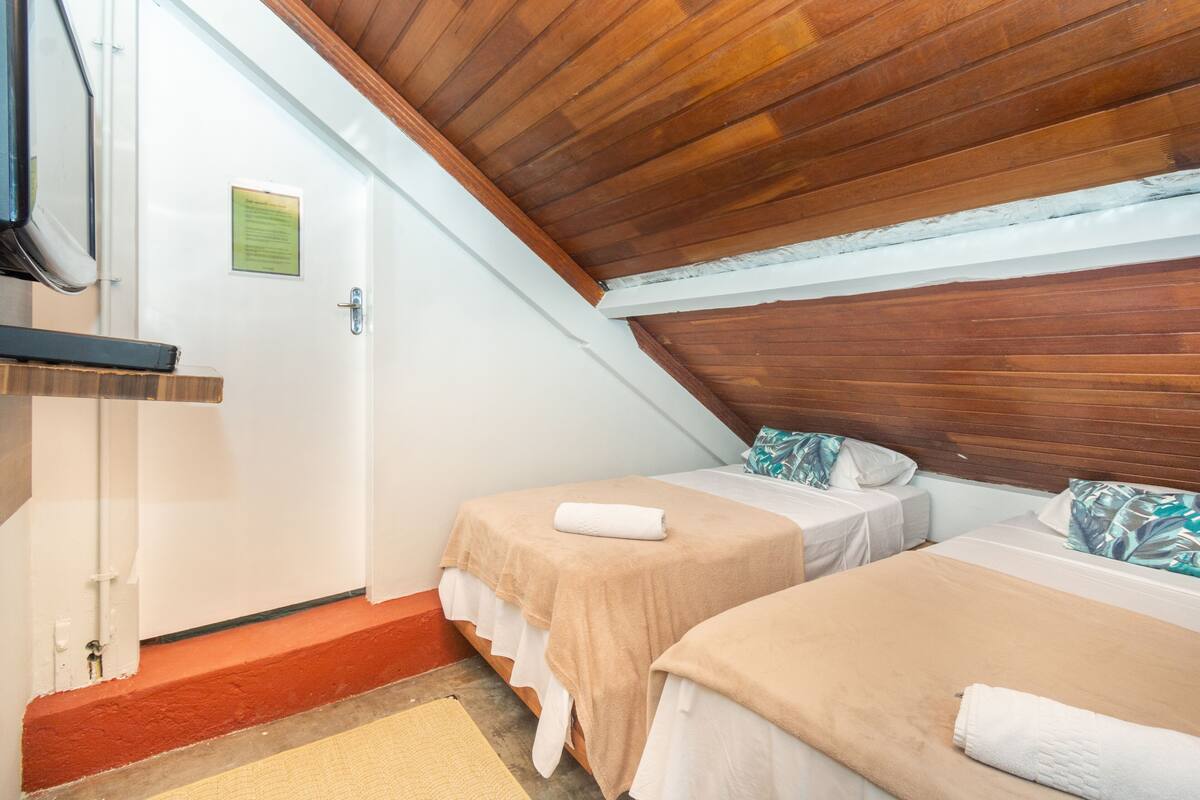 A room with two beds, wooden ceiling, and a door with a sign.