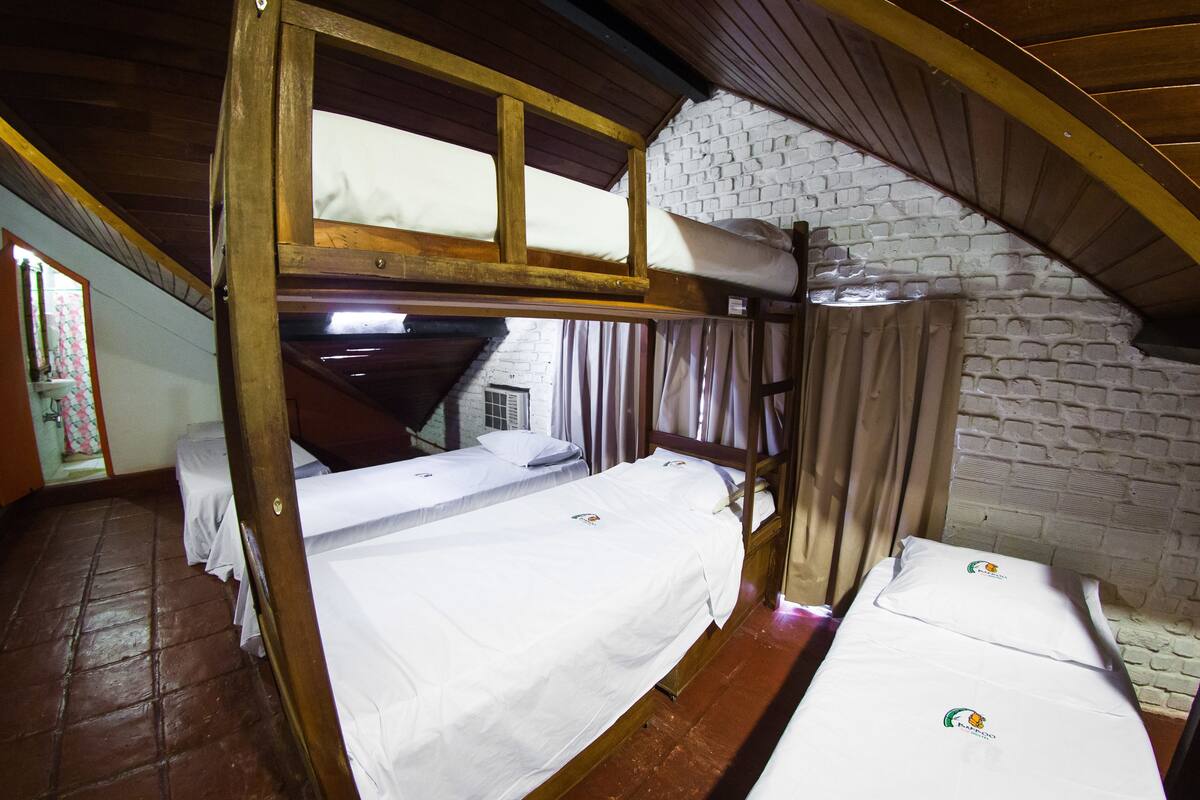 A dormitory room with bunk beds, a brick wall, and a wooden ceiling.