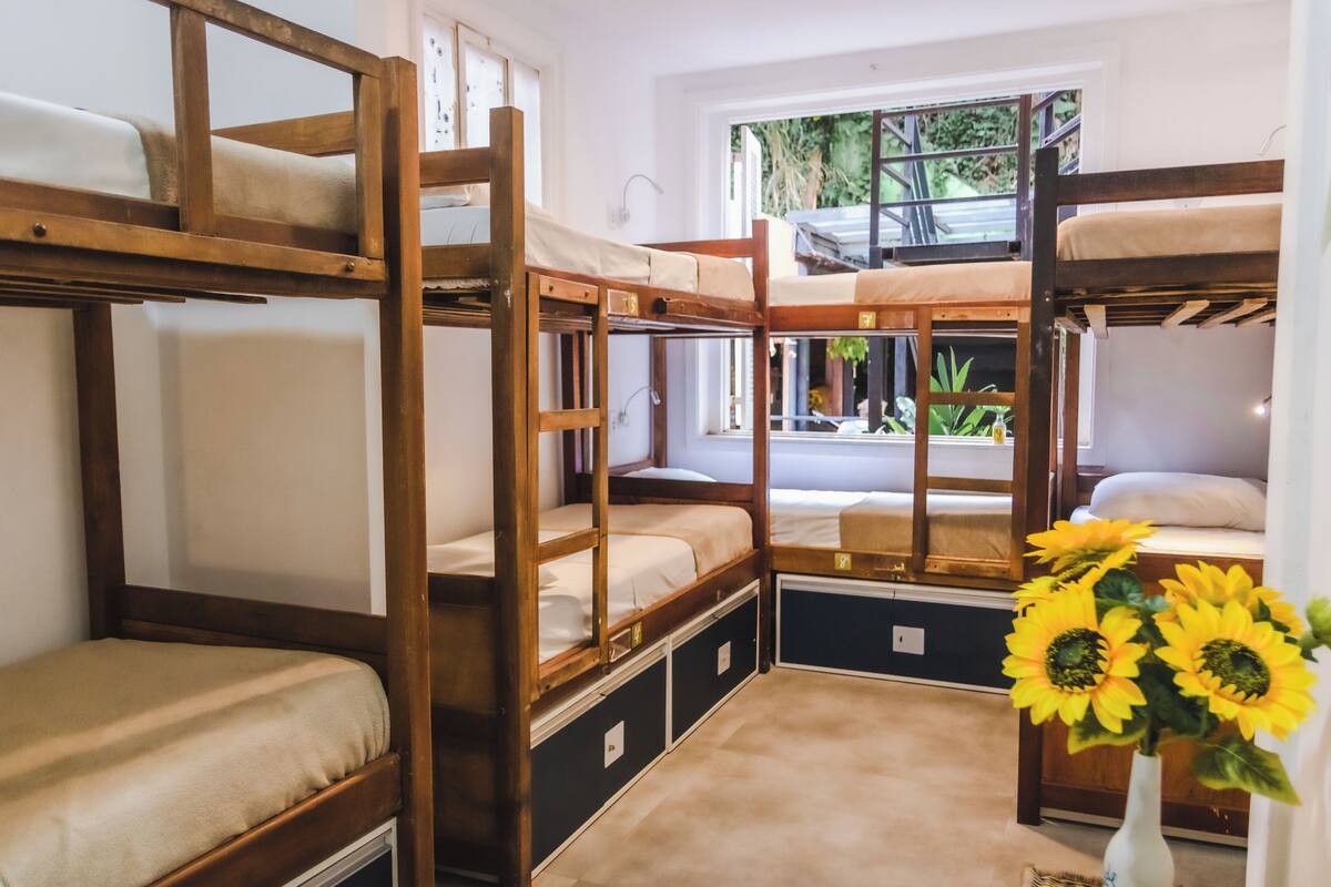 A bunk bed room with a window view, a vase with sunflowers, and a small table.