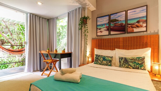 Une chambre d’hôtel avec un lit, un bureau, un hamac et une vue sur l’extérieur.