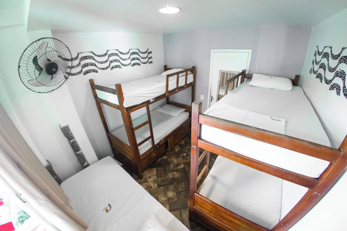 A room with three bunk beds, a wall-mounted fan, and a door.
