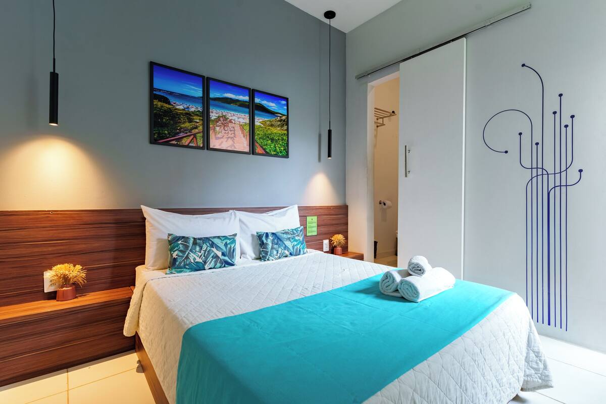 A modern hotel room with a large bed, a view of the sea, and a decorative wall piece.
