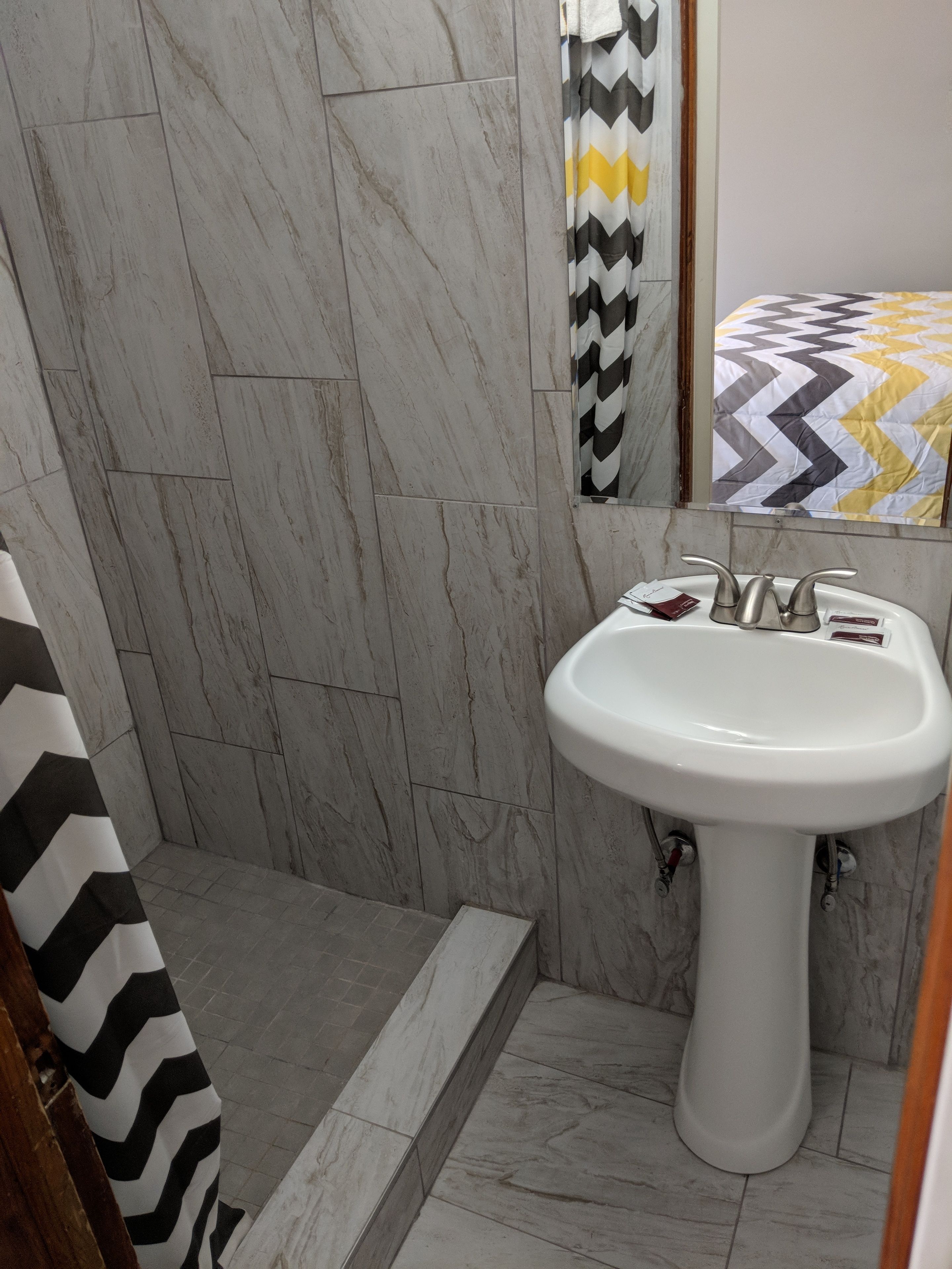 A bathroom with a white pedestal sink, a shower with a black and white chevron curtain, and a mirror above the sink.