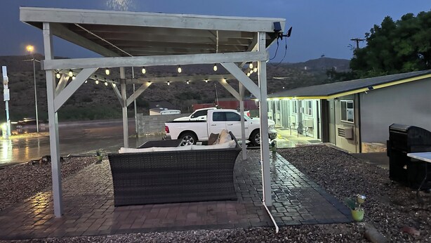 A covered outdoor area with a white pickup truck parked under a pergola with string lights. - Belle-Aire Motel (Globe)