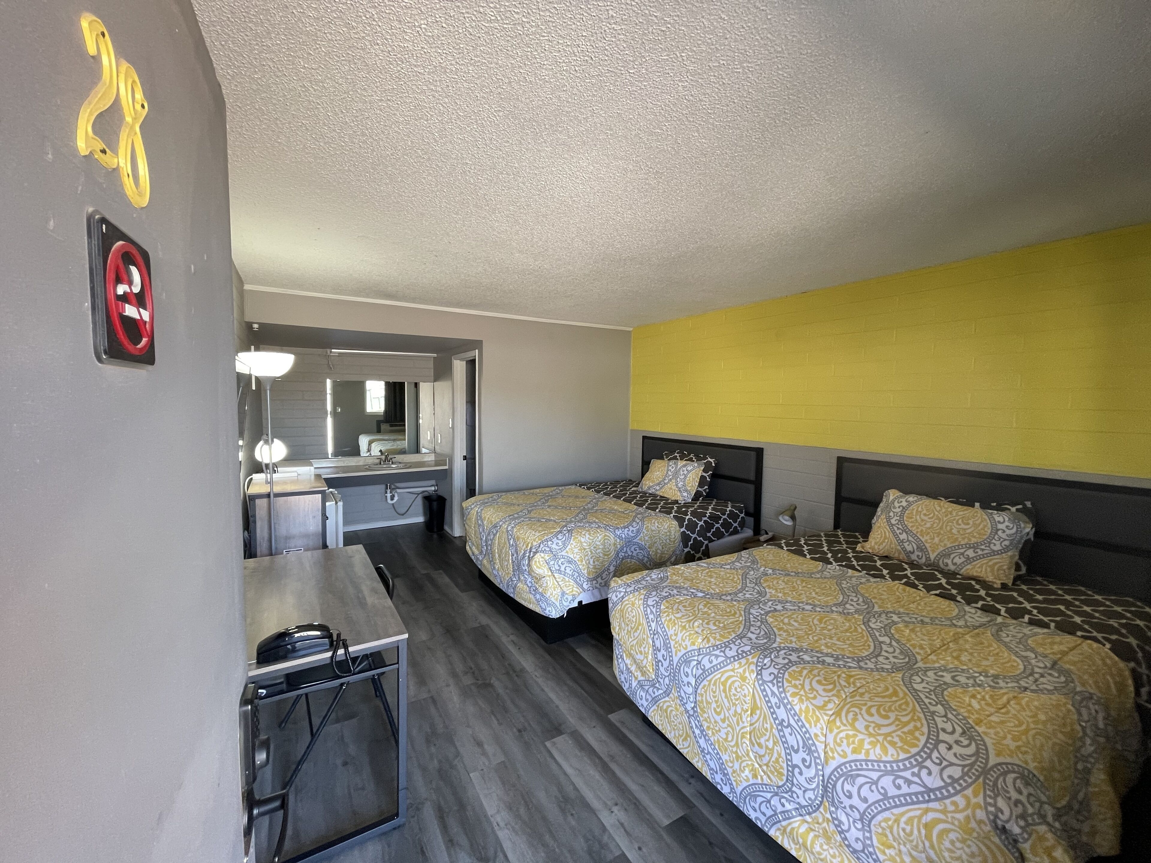 A hotel room with two beds, a desk, a mirror, and a bathroom visible in the background.