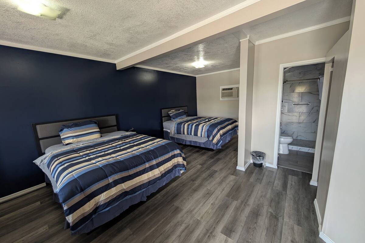 Un dormitorio con dos camas, piso de madera y baño con ducha e inodoro.