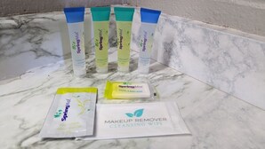 A bathroom with a marble countertop, four tubes of Spring Mist products, a facial and body soap, and a makeup remover cleansing wipe. - Belle-Aire Motel (Globe)