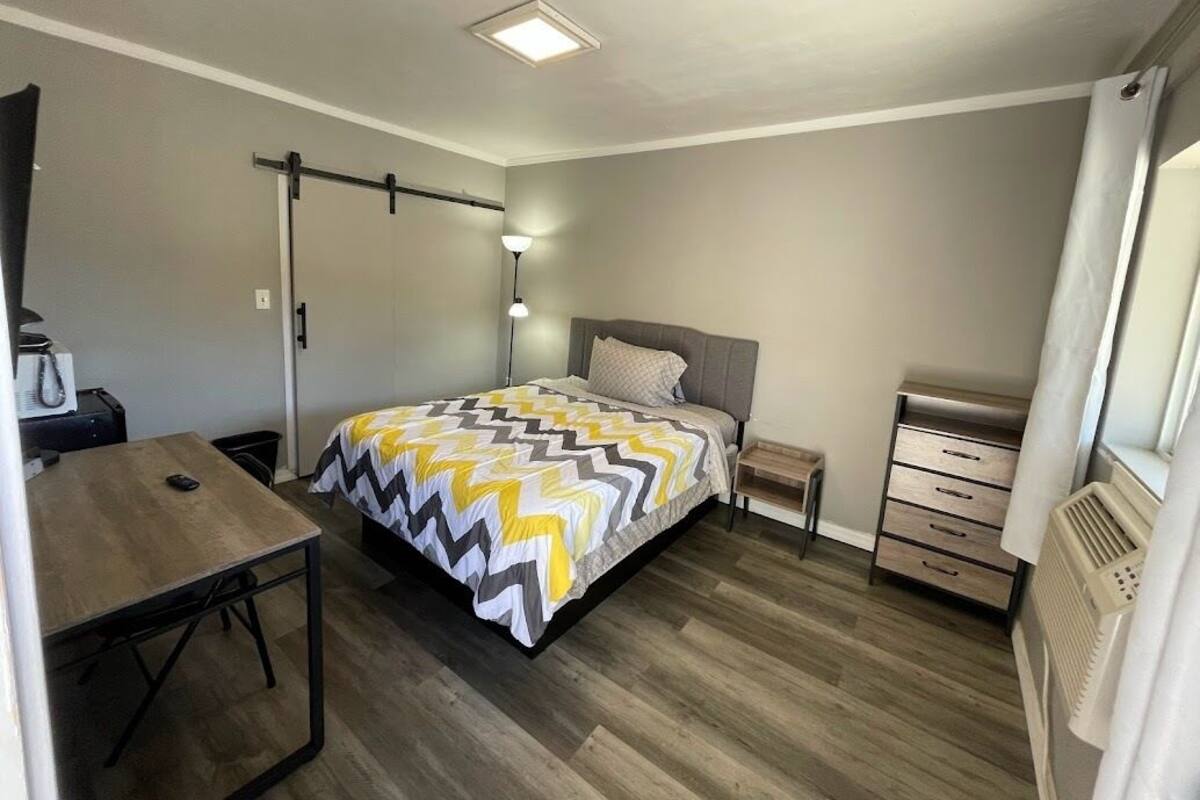Un dormitorio pequeño con cama, mesita de noche, lámpara y un escritorio.