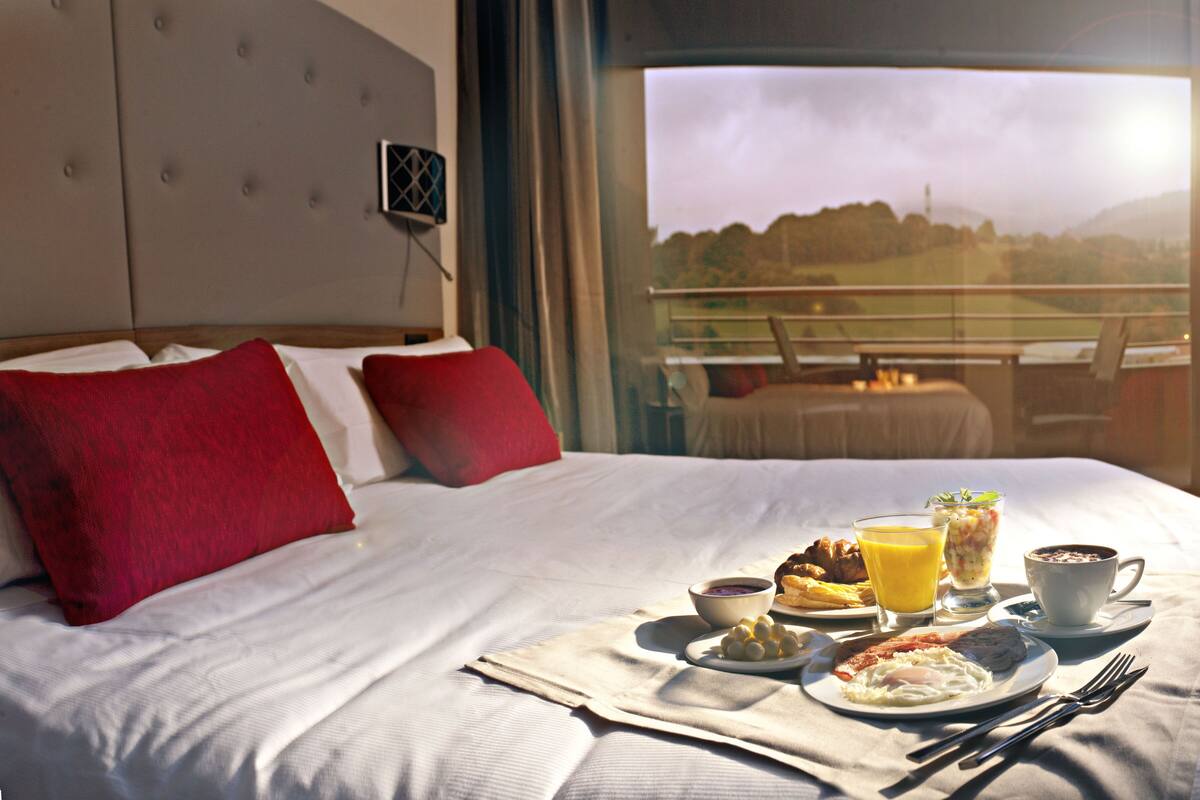 A hotel room with a bed, breakfast tray, and a view of the outdoors.