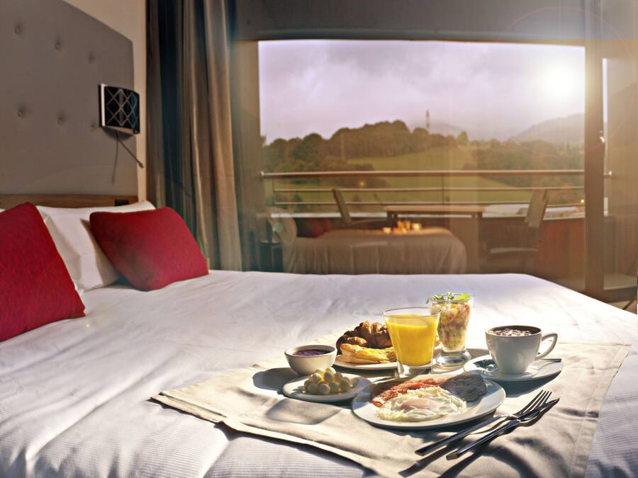 Habitación de hotel con cama, bandeja de desayuno y vistas al exterior.
