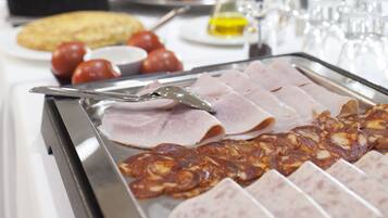En buffet med forskellige spiser, herunder kød, oste og frugt.