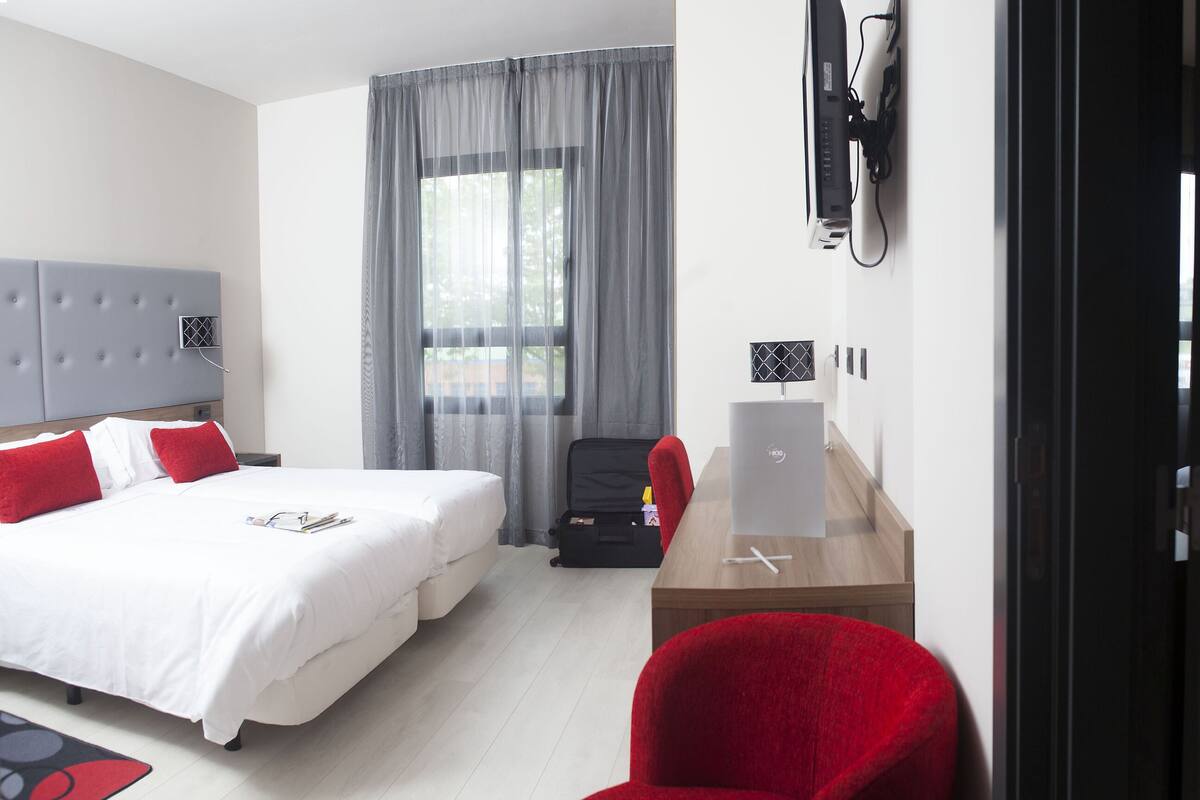 A hotel room with two beds, a desk, a chair, and a TV.