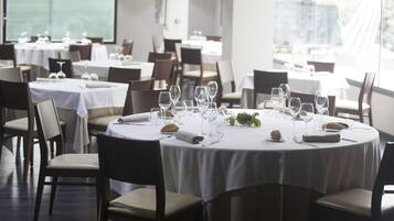 Un restaurante con mesas redondas dispuestas para comer, con manteles blancos y cubertería ordenada.