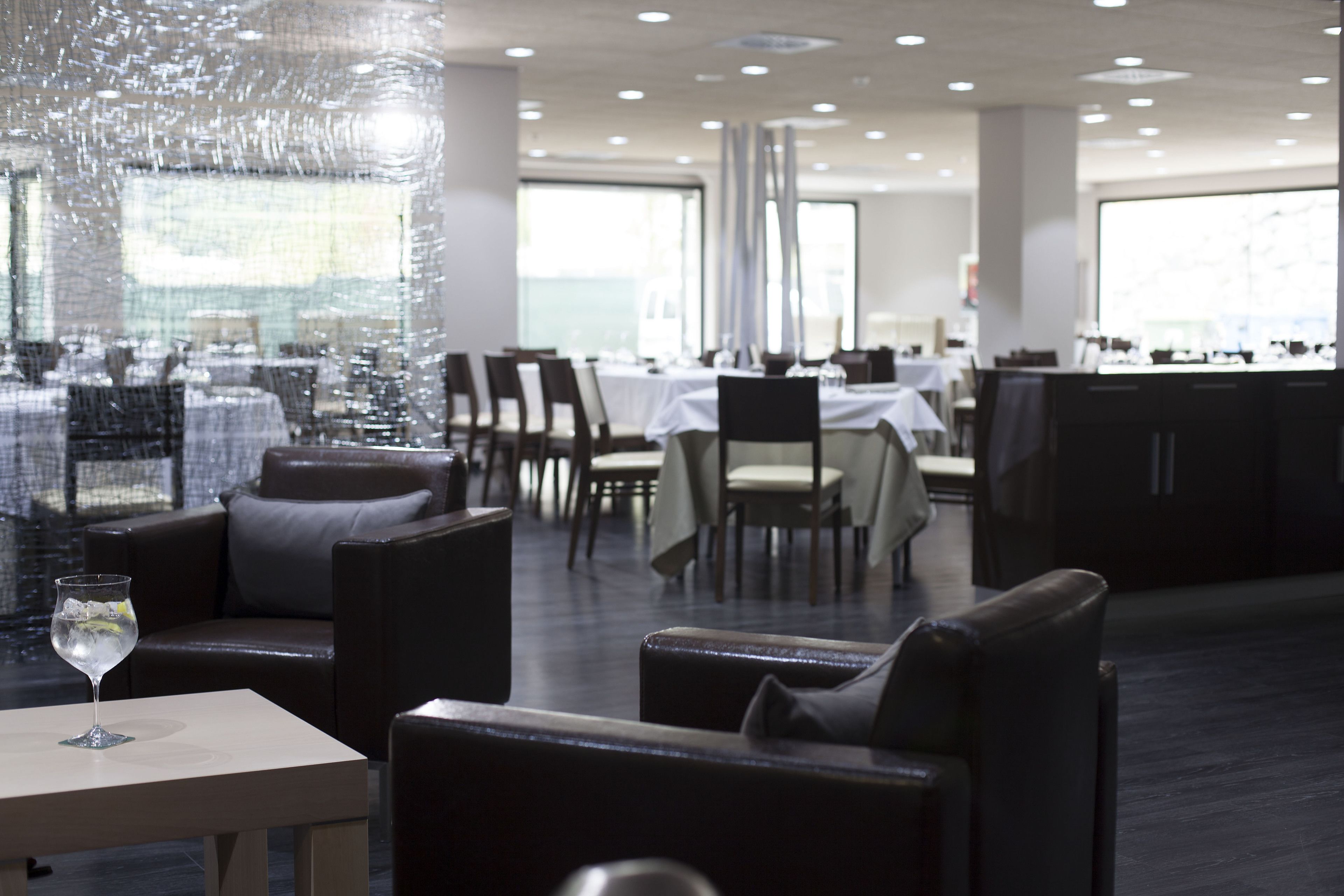A modern restaurant with leather seating, white tables, and large windows.
