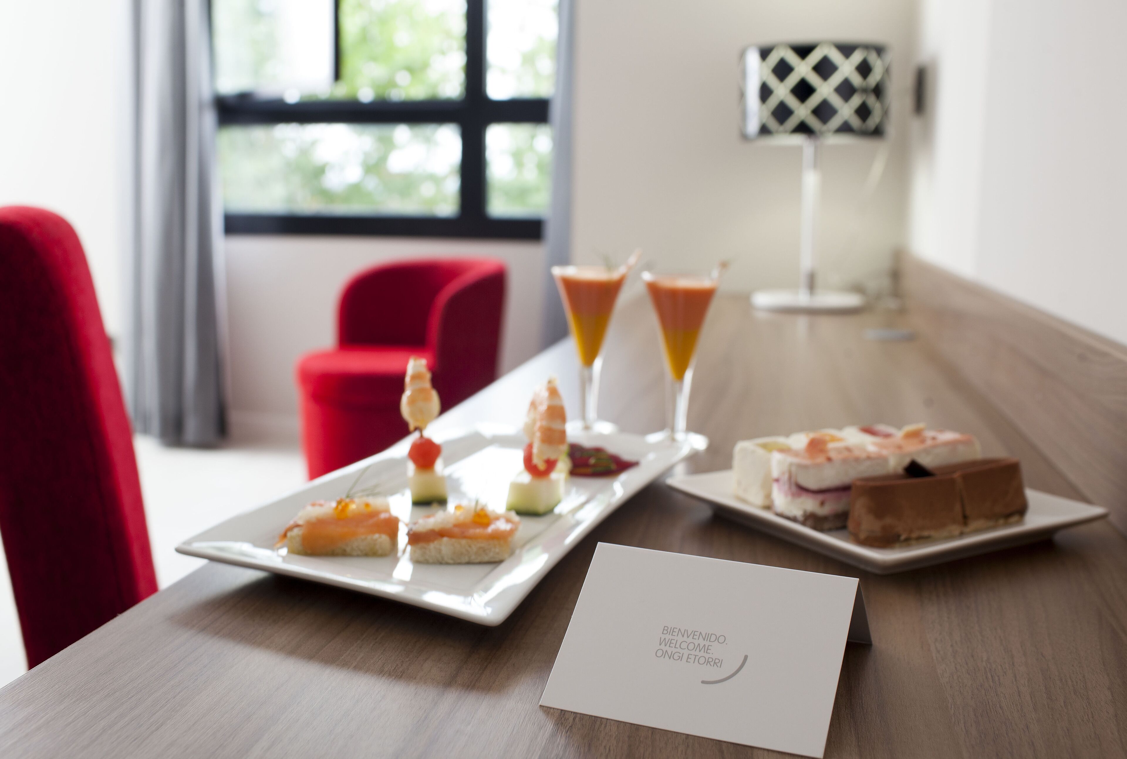 A dining table with a white plate of appetizers, two martini glasses, and a dessert plate. A welcome card is placed on the table.